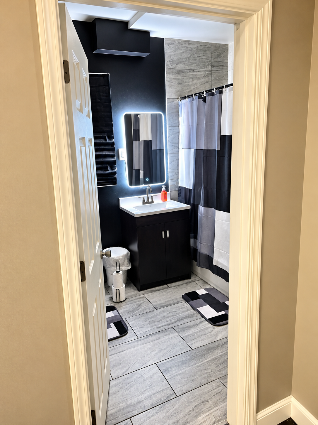 Bathroom — black vanity, illuminated mirror, black-and-white shower curtain, floor mats
